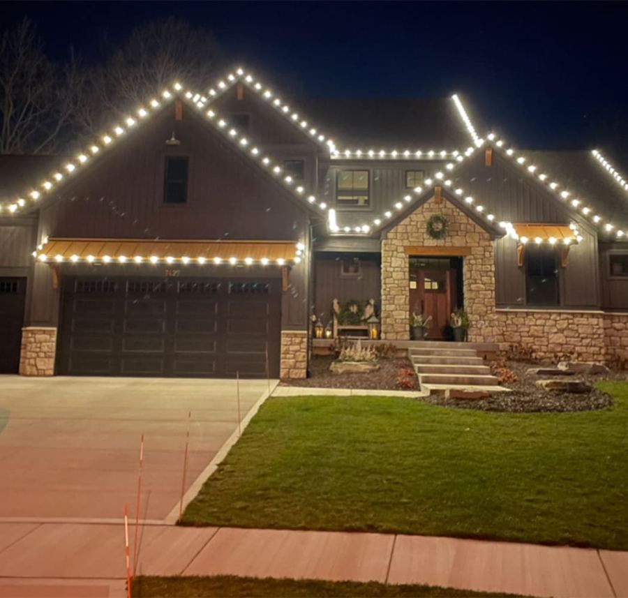 Two-story stone home with white roofline Christmas lights and a wreath