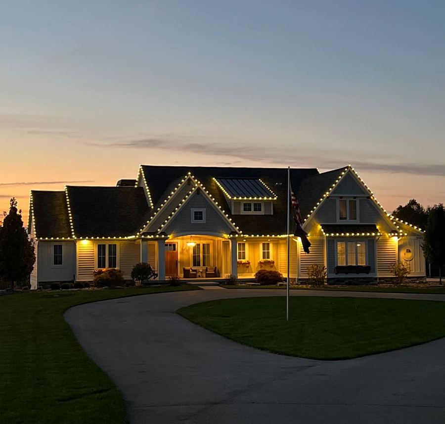 Single-story home outlined in warm white Christmas lights at dusk